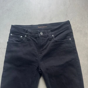Svarta Nudie Jeans Black 27/32 - Svarta jeans från Nudie Jeans. Klassisk femficksdesign med svarta sömmar och diskret logga på bakfickan. Jeansen har normal passform och är tillverkade i mjukt bomullstyg med stretch för extra komfort. Skriv gärna om du har minsta lilla fråga. Kan gå ner i pris vid snabb affär.😀