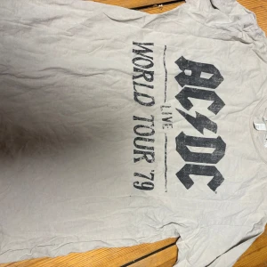 AC/DC World Tour '79 t-shirt XS - Säljer en grå AC/DC t-shirt från H&M i storlek XS. T-shirten har korta ärmar och ett stort svart tryck med texten 'AC/DC Live World Tour '79' på framsidan. Materialet är mjuk bomull och passformen är normal.