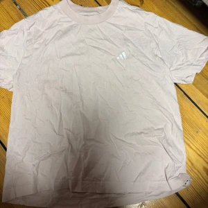 Ljusrosa Adidas t-shirt i bomull - Säljer en ljusrosa t-shirt från Adidas i storlek M. T-shirten har klassisk rund hals och korta ärmar, med en liten Adidas-logga på bröstet. Materialet är mjuk bomull och passformen är normal. Perfekt för en chill och sportig look.