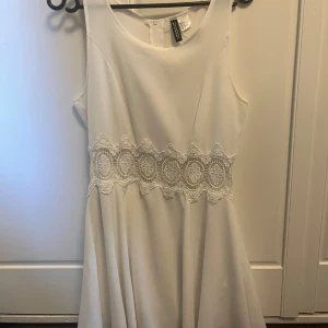 Vit klänning med spets från H&M Divided - Superfin vit klänning från H&M Divided med rund halsringning och bred spetsdetalj i midjan. Klänningen är ärmlös och har en lätt utställd kjol. Perfekt för sommarens alla tillfällen!