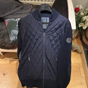 Cardigan  - Snygg mörkblå kofta från State of Art med quiltad framsida och ribbstickade ärmar. Dragkedja framtill, två fickor med dragkedja och quiltade armbågslappar. Perfekt för lager-på-lager och stilren look.