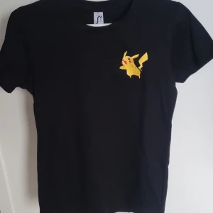  Helt ny Svart Pikachu t-shirt från SOL'S - Helt ny Svart t-shirt med en broderad Pikachu på bröstet. T-shirten är av modellen SOL'S Imperial Women.Det stor storlek S men den är XS  100% bomull