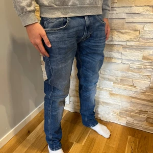 Replay Anbass jeans blå herr - Snygga blå Replay Anbass jeans med klassisk femficksdesign och raka ben. Jeansen har en mörkblå tvätt med lätt slitning och kontrastsömmar. Skön passform och stilren look, perfekta till sneakers eller boots. W33/L32