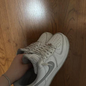 Nike Air Force 1 vita sneakers med grå nikelogga - Klassiska Nike Air Force 1 sneakers i vitt skinn med grå swoosh. Modellen har perforerad tå, snörning och platt sula. Perfekta för dig som gillar en clean och tidlös look. Passar till det mesta och är riktigt bekväma att ha på sig. Den har st 41 och kostade 1500kr ny, och jag lägger ut dessa för 600kr men priset är inte hugget i sten. Man får också med original boxen.