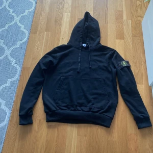 Svart hoodie från Stone Island - Svart hoodie från Stone Island med klassisk patch på vänster ärm. Tröjan har huva med snörning och en stor magficka. Tillverkad i mjuk bomull och har långa ärmar med ribbade muddar. Perfekt för en chill och stilren look. Pris kan diskuteras 