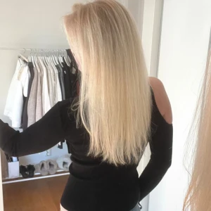 Svart ribbad topp med öppen axel - Snygg svart ribbad topp med lång ärm och öppen axel på ena sidan. Figurnära passform som framhäver siluetten och ger en trendig look. Perfekt att matcha med jeans eller kjol för en cool stil.