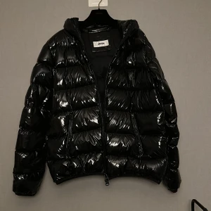 Svart pufferjacka från Grifoni - Säljer en svart, glansig pufferjacka från Grifoni. Perfekt för kalla dagar. Passformen är normal och jackan är helsvart utan mönster. Säljer den för 1499kr (nypris 6000) Den har en liten slitning på höger axel, kom privat för info/bild om det.