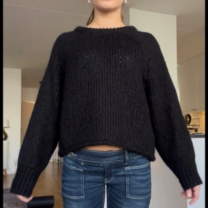 Svart stickad tröja med loose fit - Mysig svart stickad tröja med grov struktur och rund hals. Tröjan har lång ärm och en lite loose passform som ger en avslappnad vibe. Perfekt att slänga på sig när det är kallt ute.