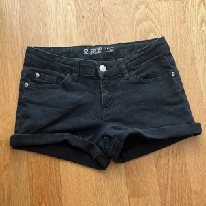 Svarta jeansshorts från Cubus - Svarta jeansshorts från Cubus med klassisk femficksdesign, uppvikta benslut och justerbar midja på insidan. Snygg och enkel modell som passar perfekt till sommaren. Gjorda i mjukt denimtyg för en bekväm känsla.