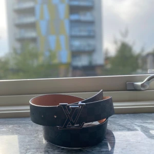 Louis Vuitton Damier skärp svart - Snyggt Louis Vuitton bälte i svart med klassiskt damier-rutmönster och silverfärgat LV-spänne. Utsidan är i präglat skinn och insidan i ljust naturfärgat läder. Perfekt accessoar för att lyfta din outfit med exklusiv känsla. Dunder kvalite, med skön tyg och passar till allt 