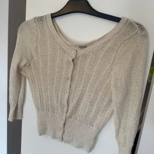 Beige kofta med spetsmönster och knappar - Söt beige kofta med spetsinspirerat stickat mönster och pärlemorknappar framtill. Långärmad och figurnära passform.