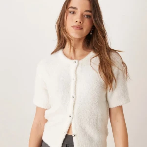 Vit fluffig kofta från Gina Tricot - Supermjuk och fluffig vit kofta från Gina Tricot med kort ärm och rund hals. Koftan har knappar framtill och är stickad i ett mysigt material som känns lyxigt. Perfekt att slänga på sig för en chill look.