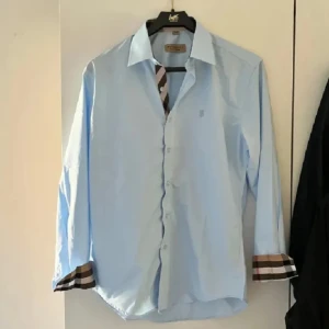 Ljusblå skjorta från Burberry - Snygg ljusblå skjorta från Burberry med klassiska rutiga detaljer på insidan. Storlek L men sitter som M nästan aldrig använd så väldigt bra skick!