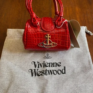 Röd handväska från Vivienne Westwood - Säljer nu denna Vivienne Westwood handväskan som skulle vara en present till mitt ex. Den är helt ny och det ingår en tyg påse och en kedja som går att knipsa fast i väskan. Skriv privat vid fler frågor.
