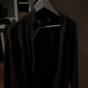 Svart Kashmir kofta från GANT med dragkedja - Svart kofta från GANT med diskret logga på bröstet. Koftan har lång ärm, ribbad krage och dragkedja framtill. Perfekt för lager-på-lager och enkel att matcha med olika outfits.