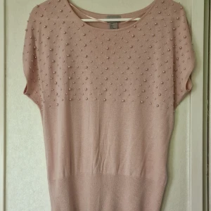 Pärlprydd ljusrosa finstickad topp - Superfin ljusrosa finstickad topp från H&M med pärldetaljer över axlar och bröst. Tröjan har korta ärmar och en avslappnad passform. Perfekt för dig som gillar söta detaljer och en mjuk känsla.