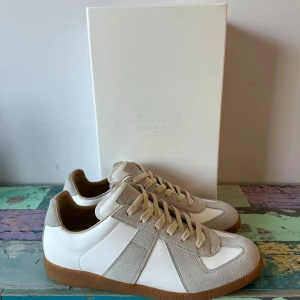 Äkta Maison Margiela GAT - Säljer ett par riktigt fräscha och trendiga Maison Margiela GAT skor i storlek 43, men passar 42 också. Skorna är en ”off White” färg. Aldrig använda. Nypris ligger runt 6000kr.Till köp nedkommer box och tyg dustbags. De är i oanvänt skick och säljer då de inte passade mig så bra. Kom gärna vid funderingar och jag är öppen för prisförslag.