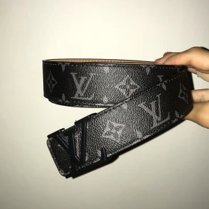  svart bälte med monogram - Snyggt svart bälte i skinn med klassiskt monogrammönster i grått. Bältet har en lyxig känsla och insidan är ljusbeige. Perfekt accessoar för att lyfta din outfit. Storlek kan ändras 