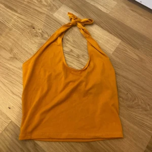 Gul halterneck linnetopp med knyt - Snygg gul halterneck linnetopp med knyt i nacken. Toppen är ärmlös och har en enkel, croppad passform. Perfekt för varma dagar och sommarvibbar. Tillverkad i mjuk bomull för en skön känsla.