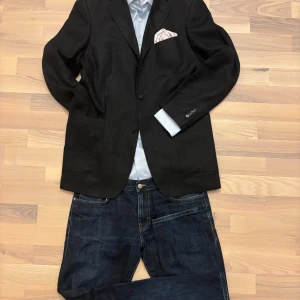 Rose&Born svart linnekavaj - Stilren svart kavaj i 100 % linne från exklusiva Rose & Born. Klassisk passform med tre knappar (2.5) framtill och en tidlös design som andas italiensk elegans. Det är en äldre modell, men inte använd mycket.  🧵 Material: 100 % linne 👔 Passform: Klassisk (48) 🎯 Detaljer: Patch-fickor, notch lapels, kissing buttons, enkel slits bak.