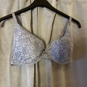 Grå spets-bh från H&M 80D - Säljer en snygg grå bh från H&M i storlek 80D. Bh:n har vacker blommig spets över hela kuporna och justerbara axelband. Den har bygel och knäppe bak. Perfekt för dig som gillar romantiska detaljer och mjuka material.