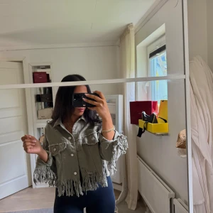 Grön croppad jeansjacka med fransar - Säljer en grön croppad jeansjacka från FB Sister med fransar längs nederkant och ärmslut. Storlek M. 250 kr