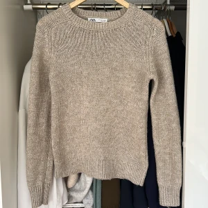 Beige stickad tröja från Zara - En stilren beige stickad tröja från Zara med rund halsringning och ribbade muddar vid ärmslut och nederkant. Tröjan har en klassisk passform och är ljusbeige i färgen. Köparen står för frakten!!💗