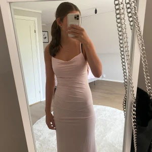 Ljusrosa långklänning med smala axelband - Supersnygg ljusrosa långklänning med smala axelband och draperad urringning. Klänningen har en tight passform och öppen rygg, vilket ger en elegant och modern look. Perfekt för dig som vill sticka ut med en stilren och feminin vibe.