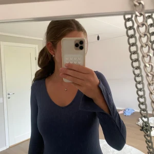 Blå ribbad långklänning med v-ringning - Säljer en blå långklänning med ribbat tyg och v-ringad hals. Klänningen har långa ärmar med lätt utsvängda ärmslut och sitter figurnära. Perfekt för dig som gillar en stilren och enkel look.