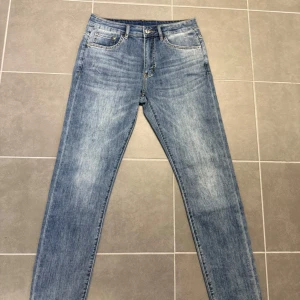 Blå jeans från Yves Saint Laurent - Snygga blå jeans från Yves Saint Laurent med klassisk femficksdesign och tydliga YSL-detaljer på knappar och nitar. Jeansen har gul kontrastsöm och är tillverkade i mjukt denimtyg. Perfekta för dig som gillar stilrena och trendiga jeans.