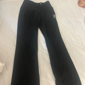 Svarta Juicy Couture mjukisbyxor XXS - Svarta mjukisbyxor från Juicy Couture i sammet med glittrande strasstenar som bildar loggan både fram och bak. Byxorna har dragsko i midjan och klassisk relaxed passform. Perfekta för en chill och trendig look.