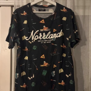 Svart Norrland t-shirt med tryck - Svart t-shirt från SOUTH CO. FROM UP NORTH med coolt Norrland-tryck och små färgglada illustrationer av natur, djur och friluftsprylar. Rund halsringning och korta ärmar. Perfekt för dig som gillar outdoor-vibes och unik stil.