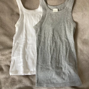 2-pack ribbade linnen från H&M XS - Säljer två ribbade linnen från H&M i storlek XS. Ett linne är vitt och det andra är ljusgrått. Båda har klassisk rak passform och ärmlös design med breda axelband. Perfekta basplagg till garderoben och superenkla att matcha med allt.