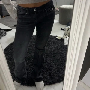 Svarta bootcut jeans - Snygga svarta jeans från Gina med bootcut passform och låg midja. Jeansen har klassiska fem fickor, silverfärgade knappar och är tillverkade i ett mjukt jeansmaterial. Perfekta för dig som gillar en stilren och tidlös look.
