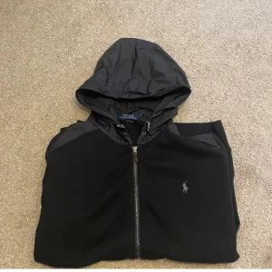 Svart Zip Hoodie från Ralph Lauren - Exklusiv zip hoodie från Ralph Lauren med dunmaterial på axlarna och luva. Perfekt nu inför våren men säljer då jag börjat tröttna på den. 