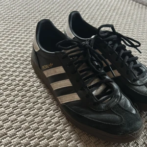 Adidas Spezial svarta sneakers strl 44⅔ - Adidas Spezial sneakers i svart skinn med vita detaljer och klassiska tre ränder på sidorna. Låg modell med snörning och gummisula. Guldtexten 'Spezial' på sidan ger en retrovibe. Perfekta för dig som gillar streetstyle och tidlös design.