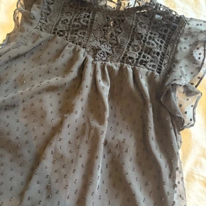 Svart blus med spets från SHEIN - Supersöt svart blus från SHEIN med transparenta prickiga partier och detaljerad spets upptill. Blusen har volang vid axlarna och är ärmlös, perfekt för att lyfta en outfit. Lätt och luftig känsla med fina broderade detaljer.