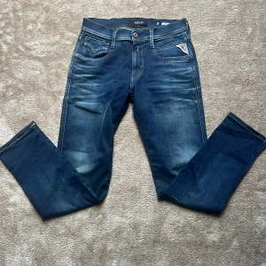 Replay Anbass jeans - Snygga blå jeans från Replay, modell Anbass. Jeansen har klassisk femficksdesign, normal passform och raka ben. Materialet är slitstarkt jeans med snygga slitningar och kontrastsömmar. Perfekta för dig som gillar en stilren och tidlös look.