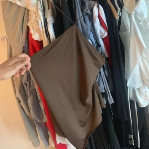 Brun asymmetrisk body - Snygg brun body  med tunna axelband och asymmetrisk skärning. Perfekt för dig som gillar minimalistisk stil och vill sticka ut med en unik form. Bodyn  är ärmlös och har en slät yta som ger en modern känsla.