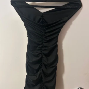 Svart halterneck klänning från SHEIN - Den sitter mycket tajtare på mig för den ör för liten men de ändå en bild hur den sitter på, den formar kroppen snyggt. Supersnygg svart kortklänning från SHEIN i storlek XS. Klänningen har halterneck, v-ringning och är axelbandslös med rynkade detaljer längs sidorna. Materialet är mjukt och stretchigt, troligtvis polyester, och sitter tight och figurnära. Perfekt för dig som gillar en stilren och trendig look.