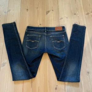 Mörkblå Replay jeans - Snygga mörkblå jeans från Replay, modell LUZ. Jeansen har klassisk femficksdesign, guldfärgade sömmar och en smal passform. Märkespatch bak i midjan och diskreta slitningar framtill för en cool look.