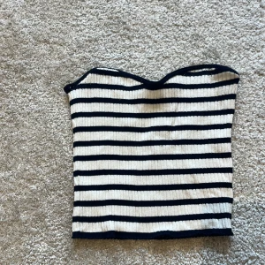 Randig ribbad tubtopp från H&M Divided - Säljer en snygg ribbad tubtopp från H&M Divided i storlek S. Toppen är vit med marinblå horisontella ränder och har en bandeauformad passning. Perfekt att styla till jeans eller kjol för en chill look.