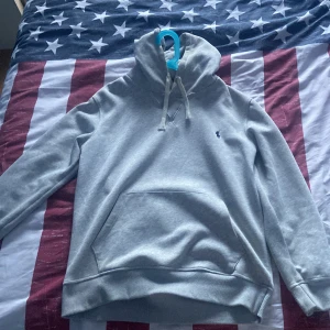 Grå hoodie från Polo Ralph Lauren - Snygg grå hoodie från Polo Ralph Lauren med klassisk broderad logga på bröstet. Tröjan har huva med snörning, känguruficka och långa ärmar. Perfekt för en chill och stilren look.