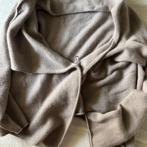 Beige stickad kofta med krage - Mysig beige stickad kofta med bred krage och enkel design. Perfekt att slänga på sig över en t-shirt eller topp. Koftan har en avslappnad passform och är tillverkad i ett mjukt stickat material.