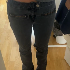 Svarta bootcut jeans med dragkedjor - Säljer ett par så coola svarta jeans med bootcut-modell och snygga dragkedjor framtill vid fickorna. Jeansen har låg midja och är tillverkade i ett klassiskt jeansmaterial. Perfekta för dig som gillar en stilren look med lite edge, dem är ganska små i storleken så passar S💞