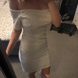 Studentklänning  - Säljer en superfin vit kort klänning med offshoulder och spetsdetaljer. Klänningen har figurnära passform och korta ärmar. Perfekt för dig som gillar romantisk och stilren look. Materialet är spets med fodrad insida. Det är en perfekt studentklänning och är i bra skick. Den går även att ha med ärmarna uppe på axlarna.