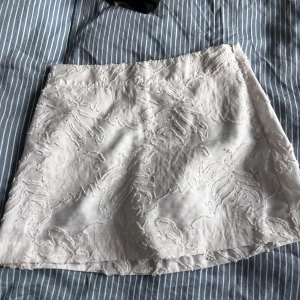 Vit kortkjol med broderade detaljer H&M - Superfin vit kortkjol från H&M med broderade mönster som ger en lyxig känsla. Kjolen har en lätt A-linjeform och är fodrad för extra komfort. Perfekt att styla med en enkel topp eller stickad tröja för en fräsch look.