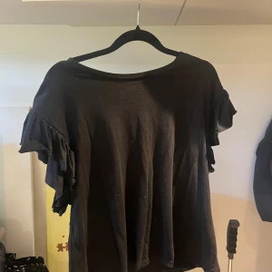 Svart volangärmad topp från Zara - Svart topp från Zara med rund halsringning och korta ärmar med volangdetaljer. Tunn och mjuk i materialet, perfekt för en chill och stilren look. Enkel att matcha med både jeans och kjol.