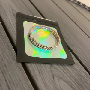 Glittrigt silverfärgat armband - Säljer ett snyggt armband i silverfärg med två rader gnistrande stenar som ger en riktigt glittrig look. Armbandet är elastiskt och passar de flesta handleder. Perfekt för dig som vill sticka ut och addera lite extra bling till din outfit en liten diamant del är sönder men annars är den jätte bra inga problem alls.