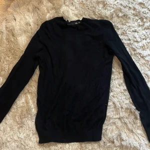 Svart långärmad stickad tröja - En svart, enkel och stilren stickad tröja Tröjan har lång ärm, rund halsringning och en smal passform. Perfekt att matcha med jeans eller kjol för en clean look.